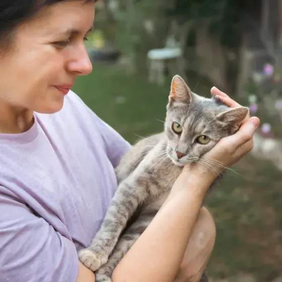 A woman holding a gray tabby cat in her arms in a garden