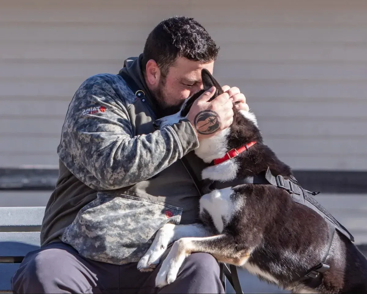 A veteran embraces his black-and-white service dog while sitting on a bench